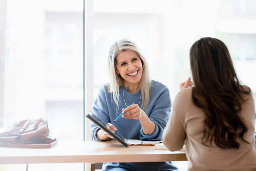 The smiling, mature adult female financial advisor meets with her unrecognizable mid adult female client to give her good news.