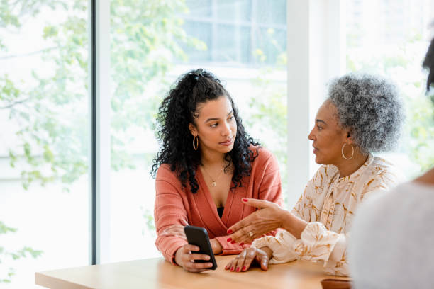 Senior mother and adult daughter have disagreement about social media The adult daughter does not like what her senior mother is saying as she shows her mother something on the smart phone. adult offspring stock pictures, royalty-free photos & images