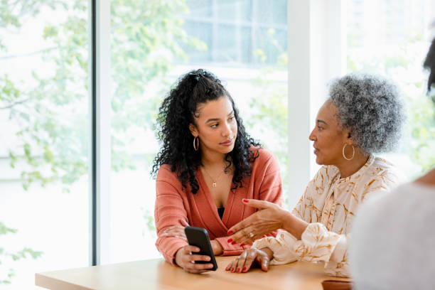 Senior mother and adult daughter have disagreement about social media The adult daughter does not like what her senior mother is saying as she shows her mother something on the smart phone. black mother and adult daughter stock pictures, royalty-free photos & images