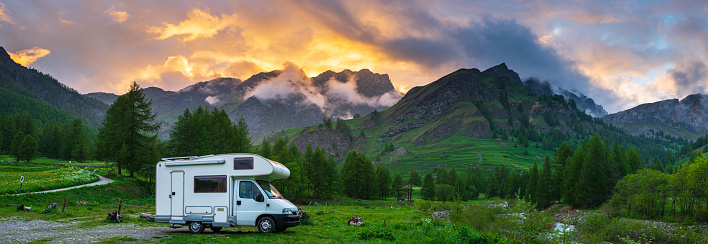 Camper van in the mountains, the Alps, Piedmont, Italy. Sunset dramatic sky and clouds, unique highlands and rocky mountains landscape, alternative vanlife vacation concept.