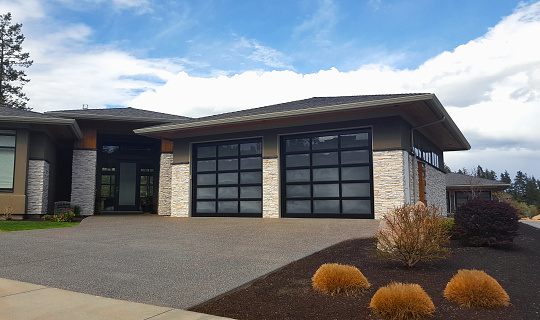 Vernon, BC, Canada- May 6, 2022: Modern Opaque glass like material on Garage Door of a home.  Modern home with stone columns, wood and concrete. Stipple stone driveway up to garage and home. Minimalism look of home garage and garden.