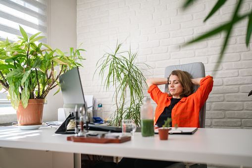 A businesswoman is sitting at office chair and taking a break and resting with her eyes closed in her office.