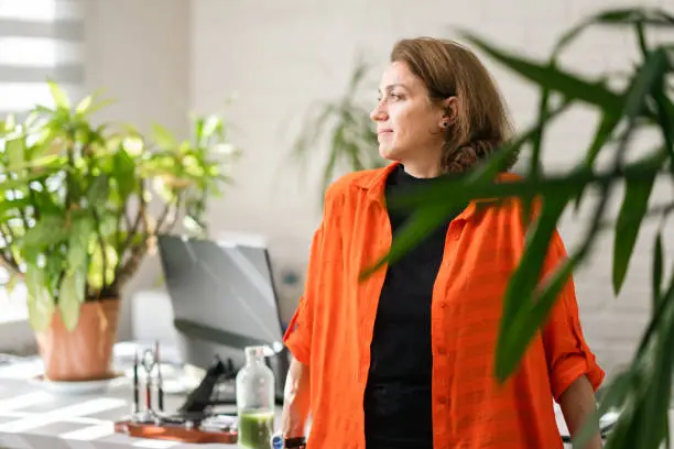 A portrait of a professional businesswoman in her environmentalist fresh green office with lots of house plants and natural light coming from windows.