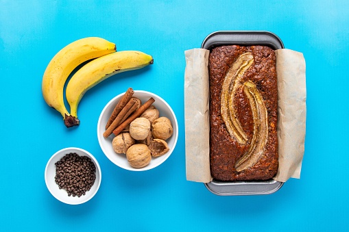 Traditional American homemade banana bread with chopped walnuts, chocolate and cinnamon in loaf pan on blue background. Fruit cake. Healthy vegan desserts concept.