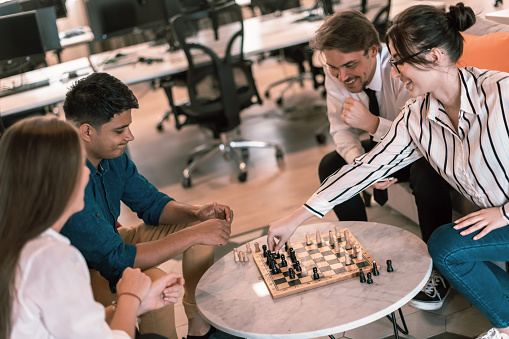 Multiethnic group of businesspeople playing chess while having a break in relaxation area at modern startup office. High-quality photo