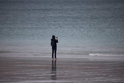 Man taking photograph with mobile phone at Luskentyre beach on the Isle of Harris, Outer Hebrides, Scotland, United Kingdom