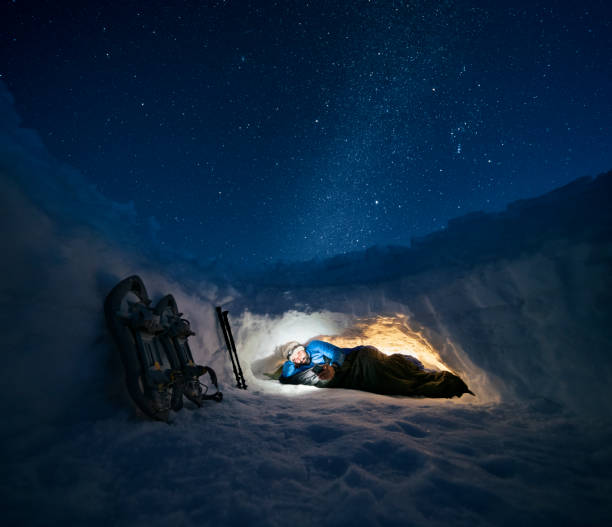 Mature tourist using phone in shelter in the snow at night. Camping in winter mountain alone in nature. stock photo