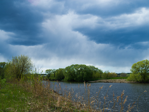 Scenic view on river, willow trees and storm clouds
