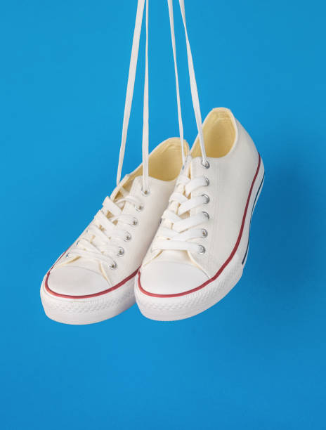 istock White sneakers with red stripes hanging on laces on a blue background. 1400350599