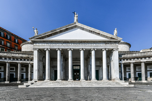 View of Basilica Reale Pontificia San Francesco da Paola church on Piazza del Plebiscito, main square of the city, and stone lion sculptures in Naples, Italy.