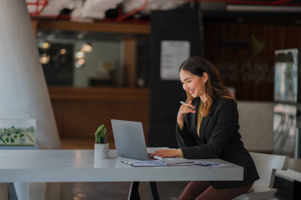 bella donna d'affari asiatica sorridente che si siede con il computer portatile e il computer che lavora sulle scartoffie fare un rapporto di analisi del conto informazioni sugli investimenti immobiliari concetti del sistema finanziario e fiscale - business seminar writing women foto e immagini stock