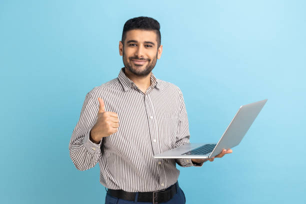 Positive businessman standing with portable computer in hand, looking at display, showing thumb up.