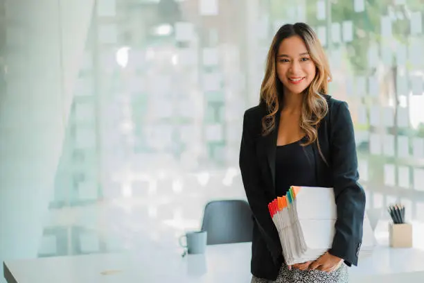 Photo of Asian businesswoman holding financial documents in front of her desk, accounting concept.