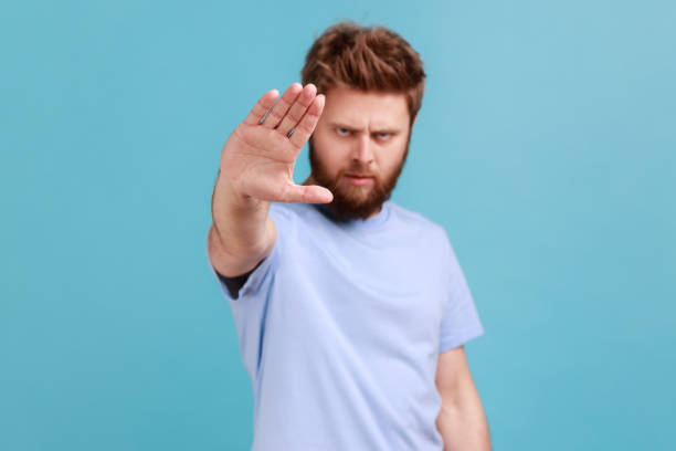 istock Man showing stop sign, standing with frowning face and bossy expression, avoid danger. 1400354705