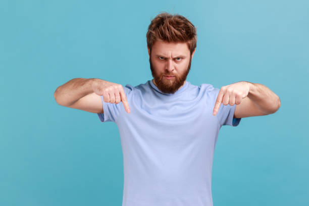 istock Man in blue T-shirt standing and looking at camera with fingers down, commanding to act here and now 1400354709