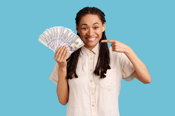 istock Woman holding dollar banknotes, pointing at cash, looking at camera with happy expression. 1400355580
