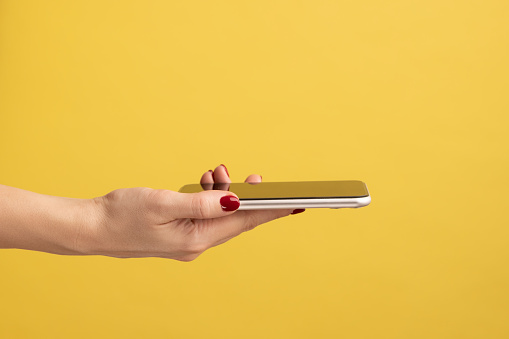 Closeup portrait of smartphone flat lying on open woman palm, female giving mobile phone. Indoor studio shot isolated on yellow background.