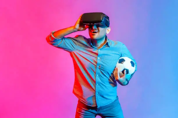 Photo of Man in shirt wearing headset and holding soccer ball, watching 3d football team.