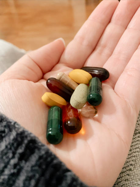 la main d’une femme post-partum tient une poignée de vitamines prises quotidiennement - probiotique, huile de poisson, prénatal, vitamine d, lécithine de tournesol et vitamine c - lecithin photos et images de collection