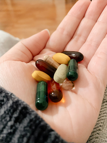 A Postpartum Woman's Hand Palm Up Holding a Handful of Colorful Vitamins That are Taken Daily - Probiotic, Fish Oil, Prenatal, Vitamin D, Sunflower Lecithin & Vitamin C.