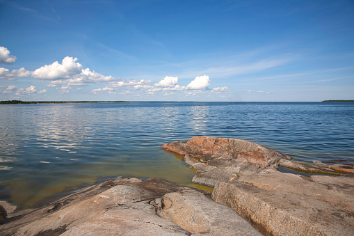 A view from a rocky shore of the Baltic Sea, with nearby islands, and beyond. Puffy clouds on a blue sky, with smooth water.
