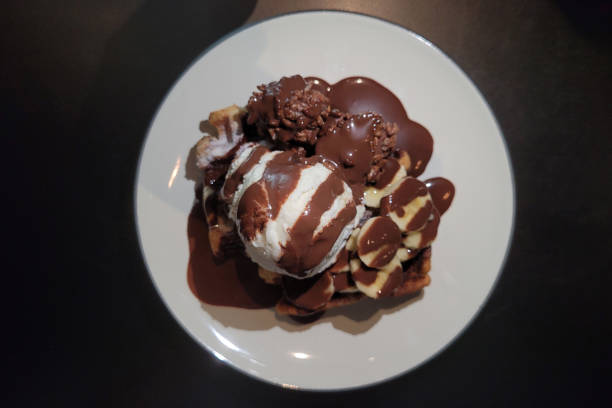 Belgium chocolate banana waffles with ice cream on a plate against black background