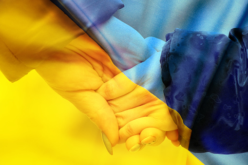 Mother holds a little girl by the hand against the background of the national flag of Ukraine yellow-blue. Peace in Ukraine, stop the war 2022