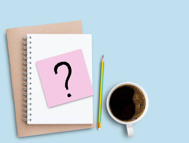istock Question mark on pink sticky note with pencil and coffee on blue table background. 1400363212