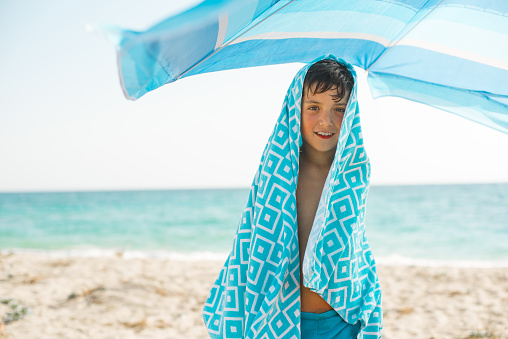 A cheerful kid on the beach on a sunny summer day wrapped in a bright beach towel.