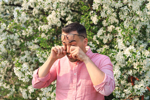 a man suffers from allergies and wipes his watery eyes