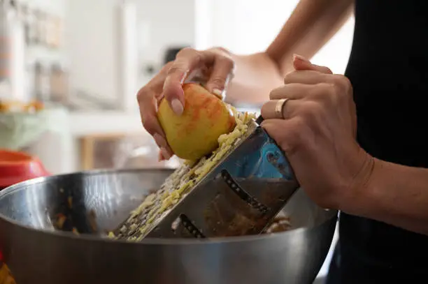 Closeup view of a woman grating an apple for apple strudel filling on a home kitchen counter.