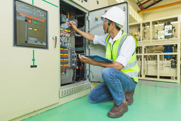 un technicien casqué tient un presse-papiers tout en vérifiant et en prenant des notes sur l’armoire de commande électrique. - electricity industry factory control panel photos et images de collection