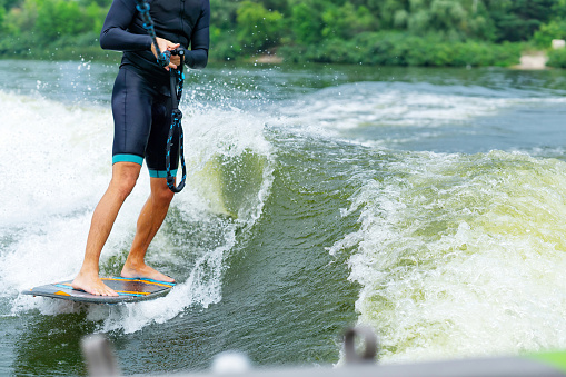 Male riding a wakeboard behind a boat on the river