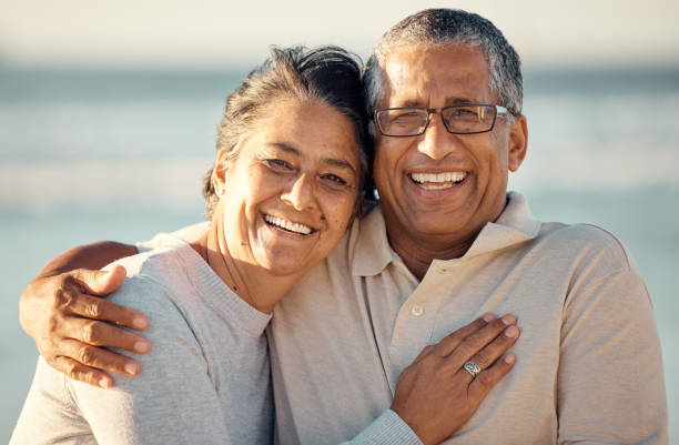 nahaufnahme eines älteren liebevollen gemischtrassigen paares, das am strand steht und während des sonnenuntergangs im freien lächelt. hispanisches paar, das liebe und zuneigung bei einem romantischen date am strand zeigt - men senior adult human face smiling stock-fotos und bilder