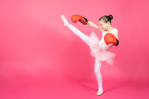 Little ballet dancer girl practicing karate. Child wearing tutu and boxing gloves isolated on vivid pink background. Female stereotype concept.