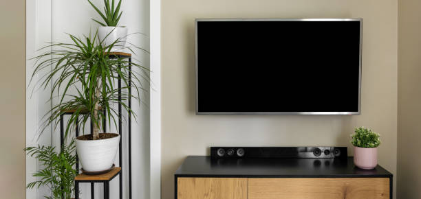 smart tv mockup hanging on beige wall in modern interior with green plants. blank screen stock photo