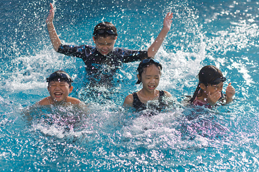 Playful little Asian boys and girls splashing happily in a swimming pool in summertime