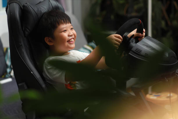 petit garçon asiatique appréciant le jeu vidéo de course automobile - amusement arcade arcade video game sport photos et images de collection