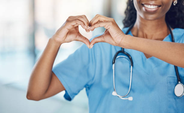 근접 아프리카 계 미국인 여성 간호사가 웃으며 병원에 서있는 동안 손으로 심장 모양을 만듭니다. 당신의 마음을 돌보고 당신의 몸을 사랑하십시오. 의학 분야의 건강과 안전 - 의사 이미지 뉴스 사진 이미지