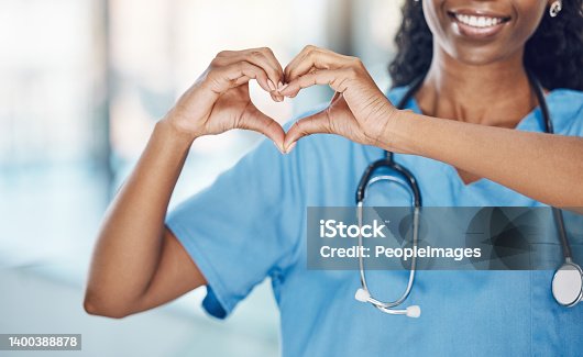 istock Closeup african american woman nurse making a heart shape with her hands while smiling and standing in hospital. Take care of your heart and love your body. Health and safety in the field of medicine 1400388878