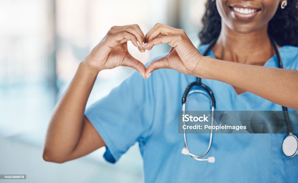 Closeup african american woman nurse making a heart shape with her hands while smiling and standing in hospital. Take care of your heart and love your body. Health and safety in the field of medicine Nurse Stock Photo