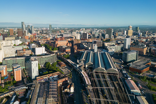 Wide angle aerial view over Manchester city centre, including Piccadilly Station and skyscrapers in the Deansgate area. Early morning sunlight.