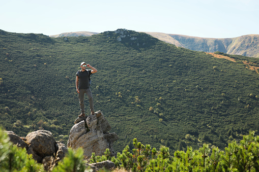 Man with backpack standing on rocky peak. Mountain tourism