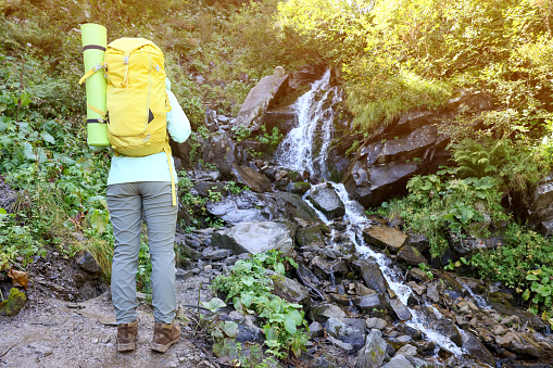 Tourist with backpack near stream in mountains, back view. Space for text