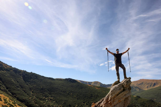 istock Man with backpack and trekking poles on rocky peak in mountains 1400391440