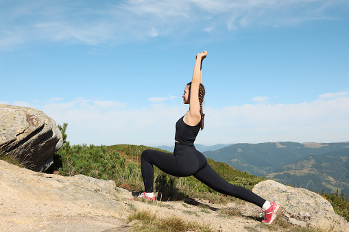Beautiful young woman stretching in mountains on summer morning