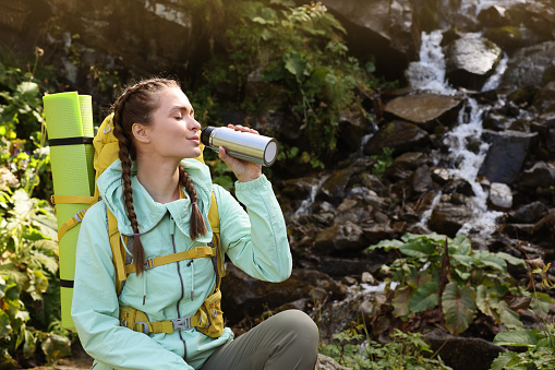 Tourist with vacuum flask near waterfall in mountains. Space for text