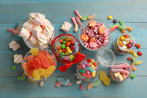 Jars with different delicious candies on light blue wooden table, flat lay