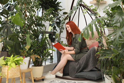 Happy beautiful woman reading book in egg chair at home