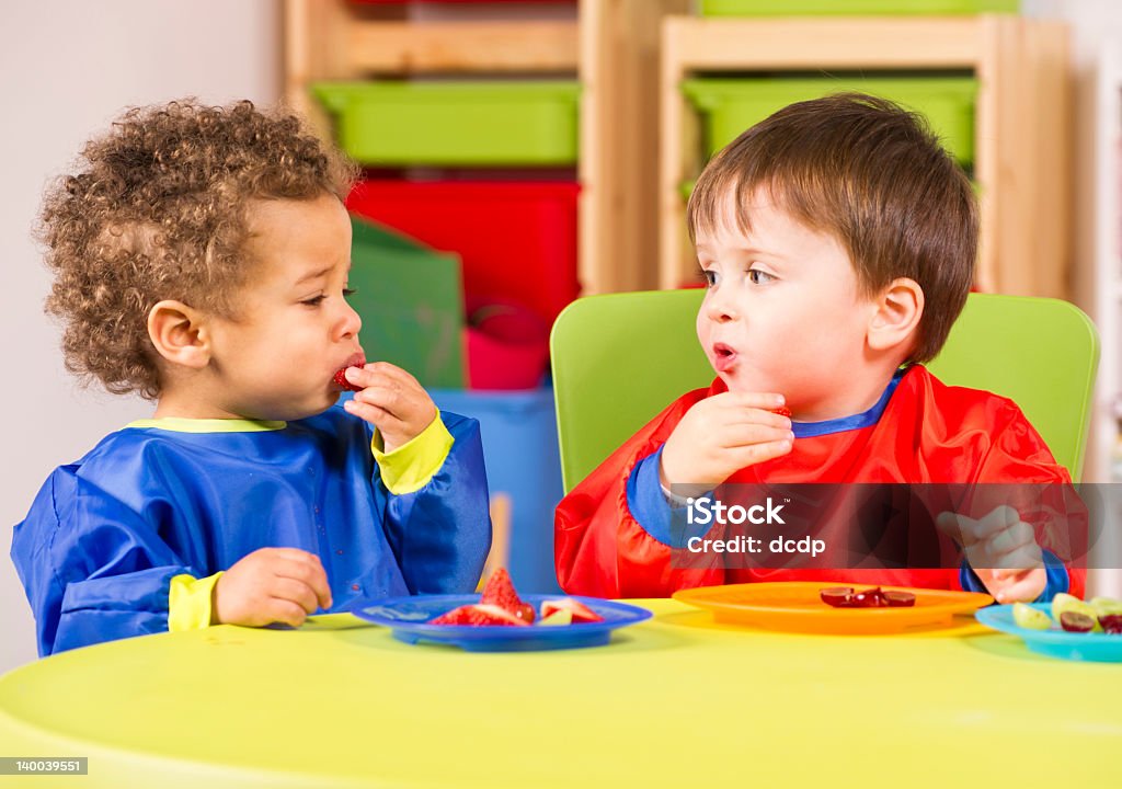 Two toddlers eating fruit in a nursery A stock photo of toddlers eating fruit and having a chat in the playroom. Eating Stock Photo